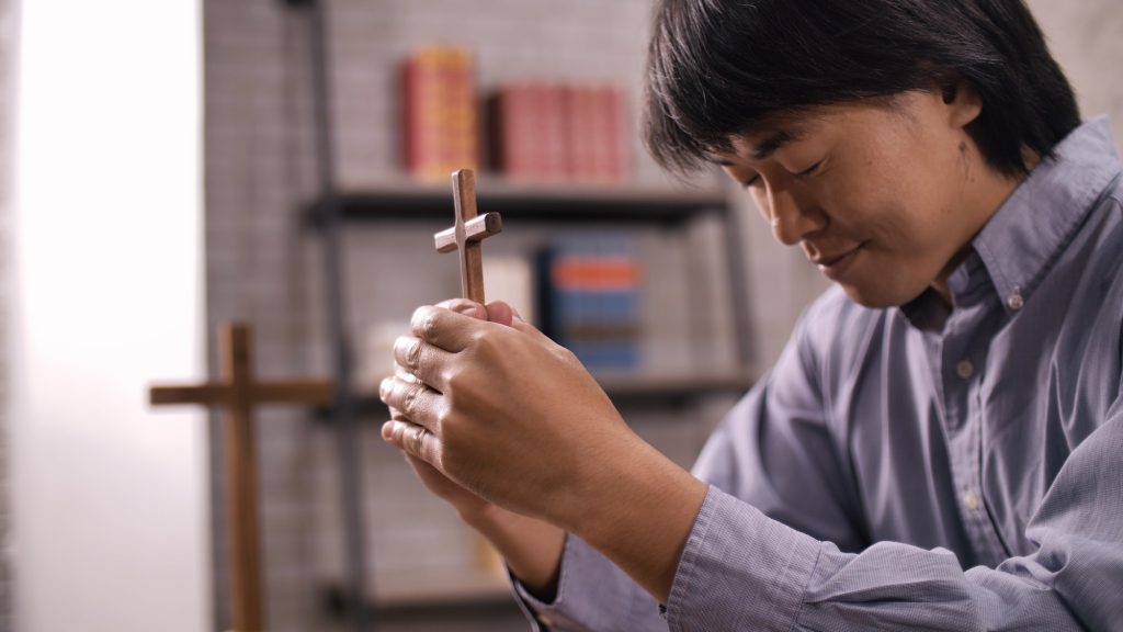 A young Asian Christian man praying to Jesus Christ in a church.